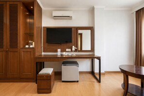 A hotel room with a wooden wardrobe, a desk with a hairdryer, a small fridge, a flat-screen TV, and a mirror. - Palette Citra Inn (Cikarang)