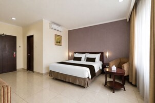 Quarto de hotel com cama, uma cadeira, mesa pequena, ar condicionado e porta.