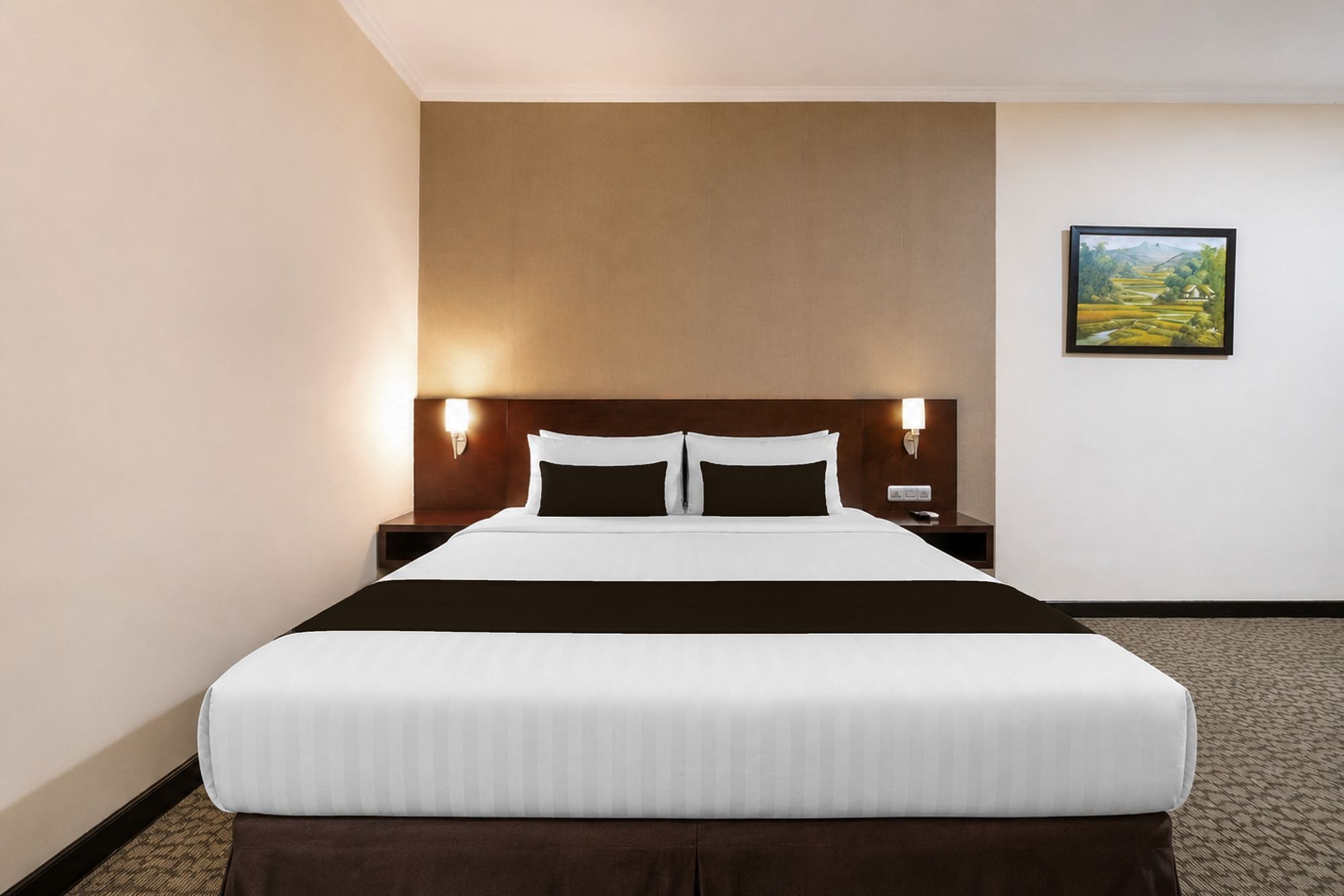 Habitación de hotel con una cama grande, dos lámparas de noche, una mesita de noche y un cuadro con paisaje en la pared.
