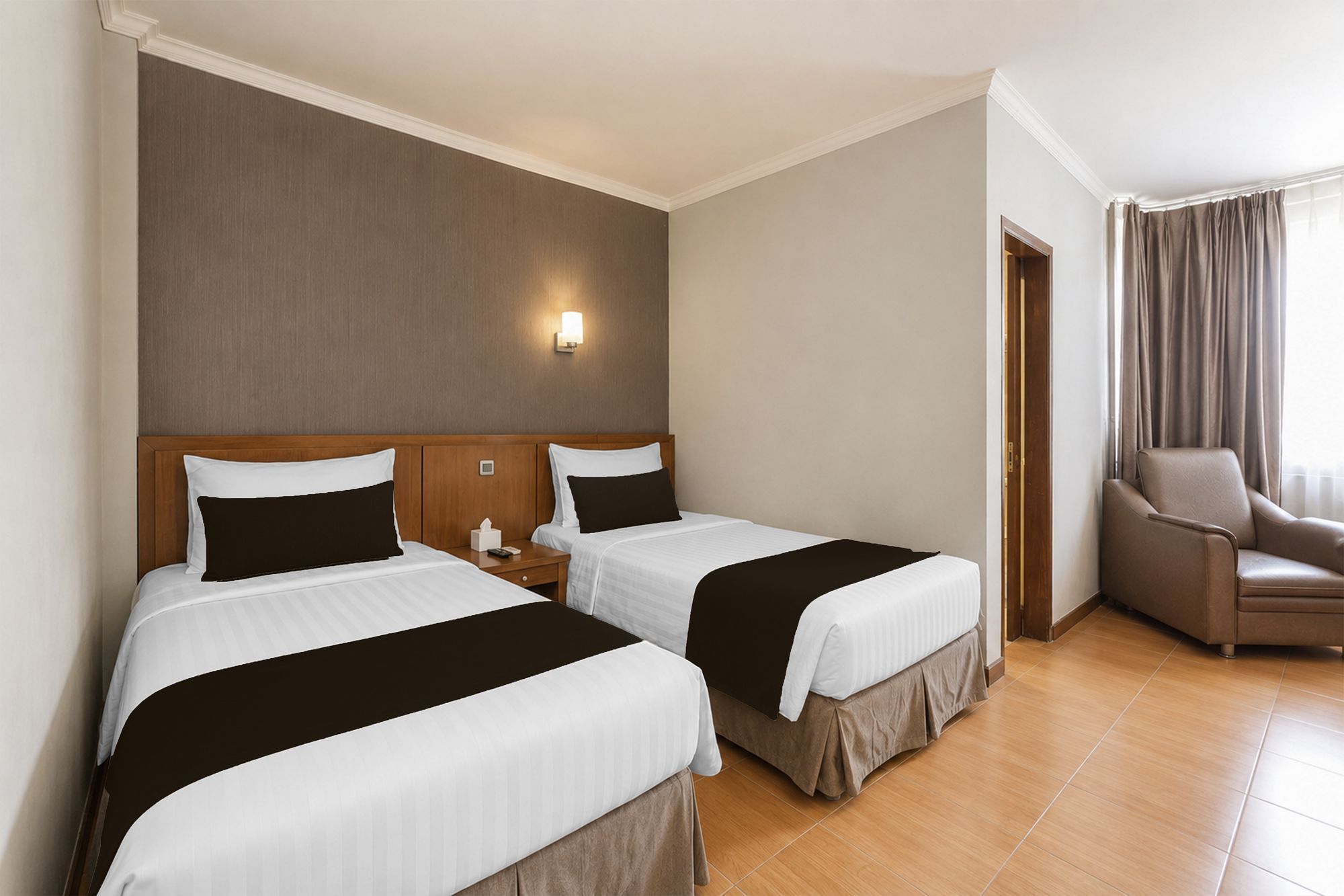 A hotel room with two beds, a nightstand, a chair, and a wall-mounted light.