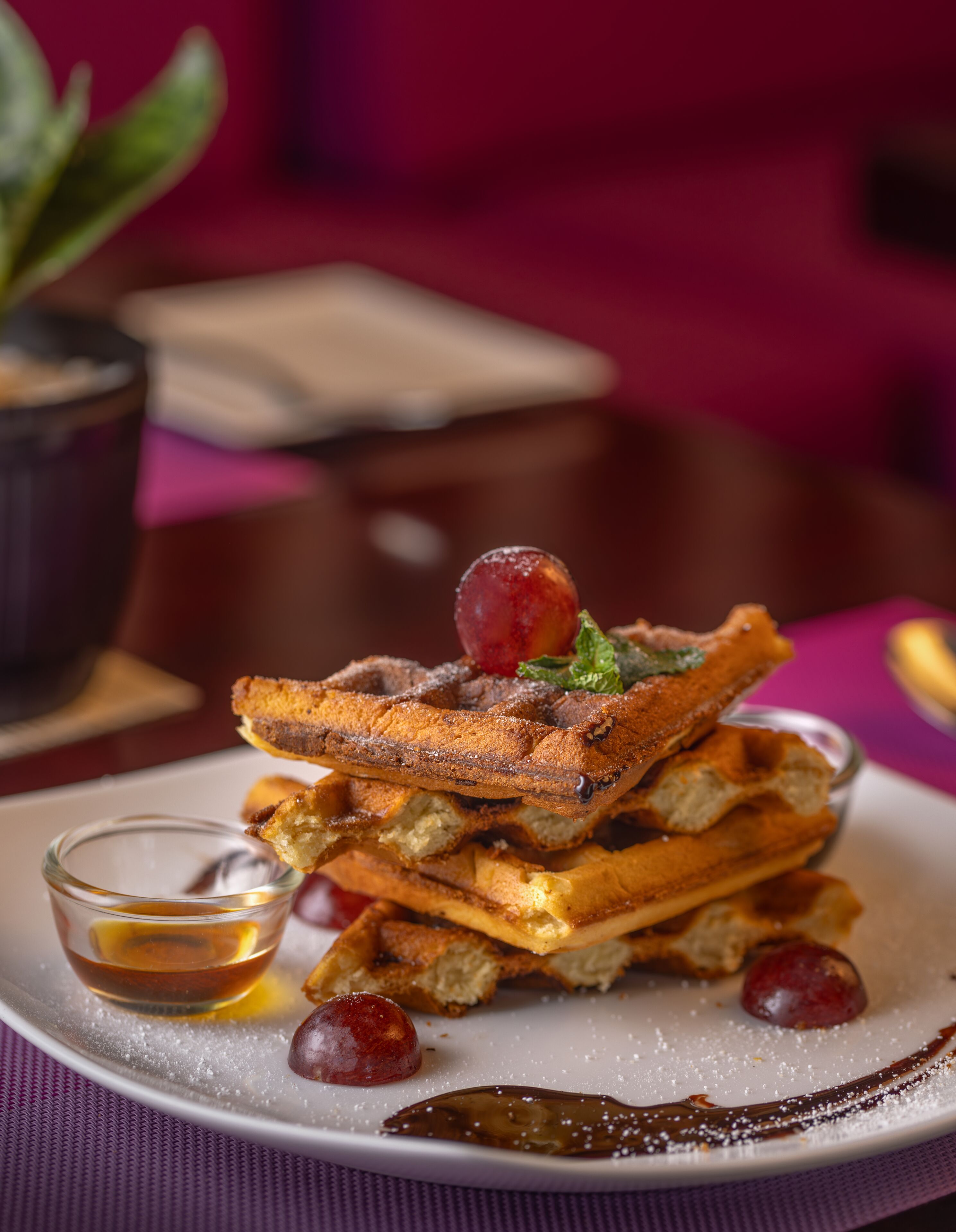 A stack of waffles with syrup and cherries on a plate.