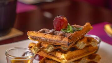 A stack of waffles with syrup and cherries on a plate.