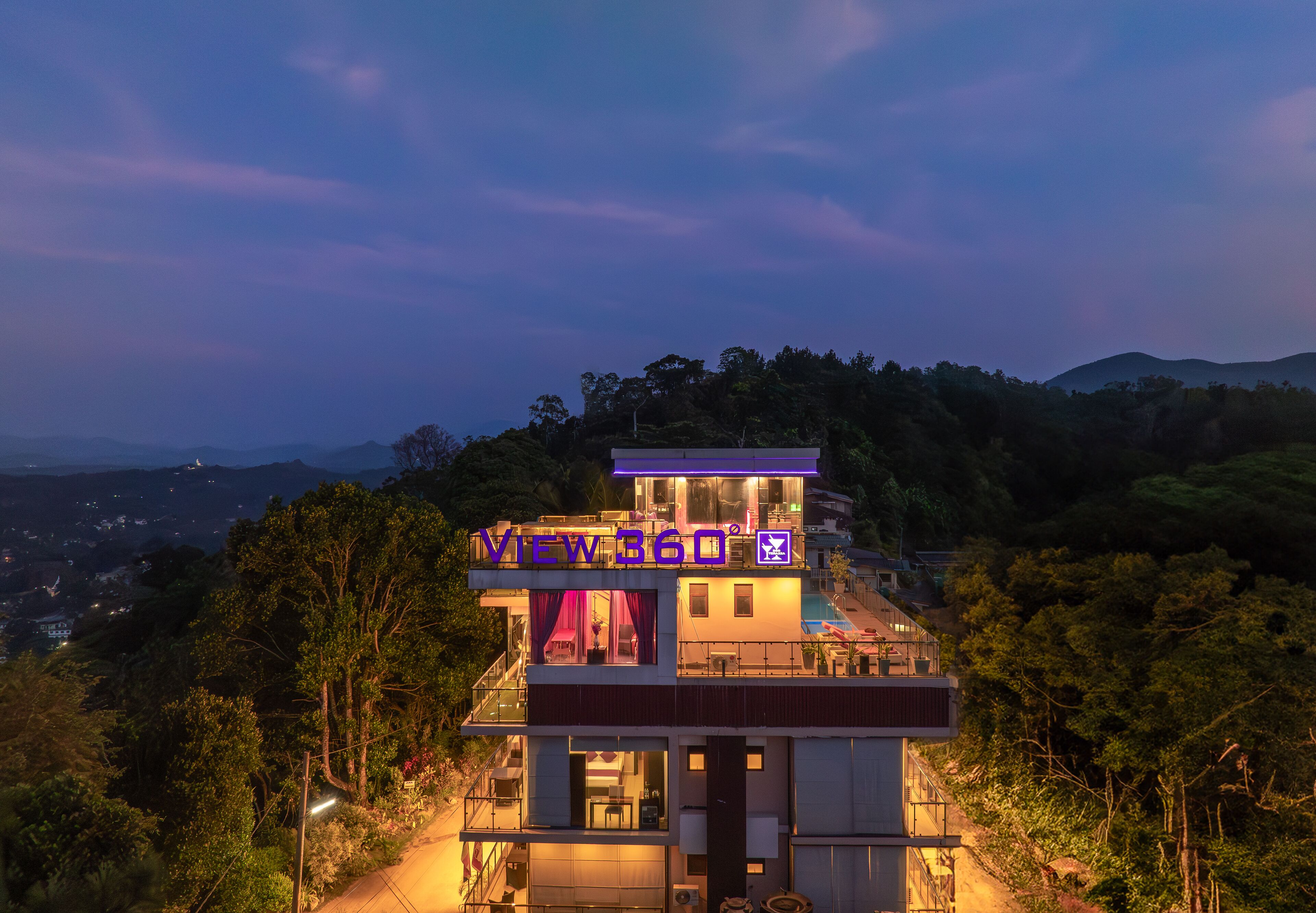 A modern hotel with a prominent "VIEW360" sign, situated on a hill with panoramic views of the surrounding landscape.