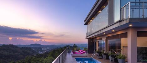 Un edificio moderno con piscina en la azotea, barandillas de vidrio y vistas al paisaje circundante.
