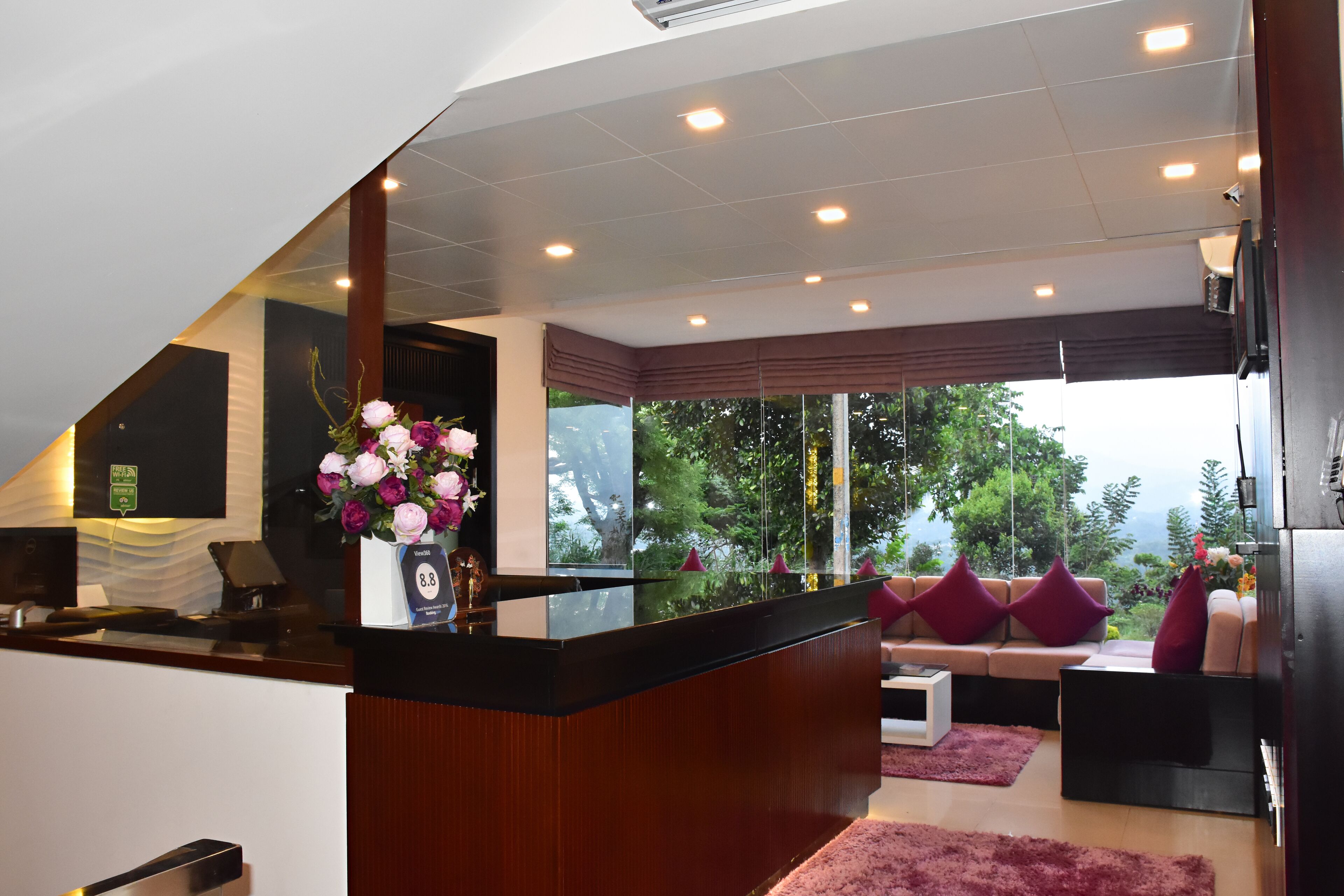 Un hall d’hôtel moderne comprenant un comptoir d’accueil, un espace salon, de grandes fenêtres offrant une vue dégagée et un mur décoratif en bois.
