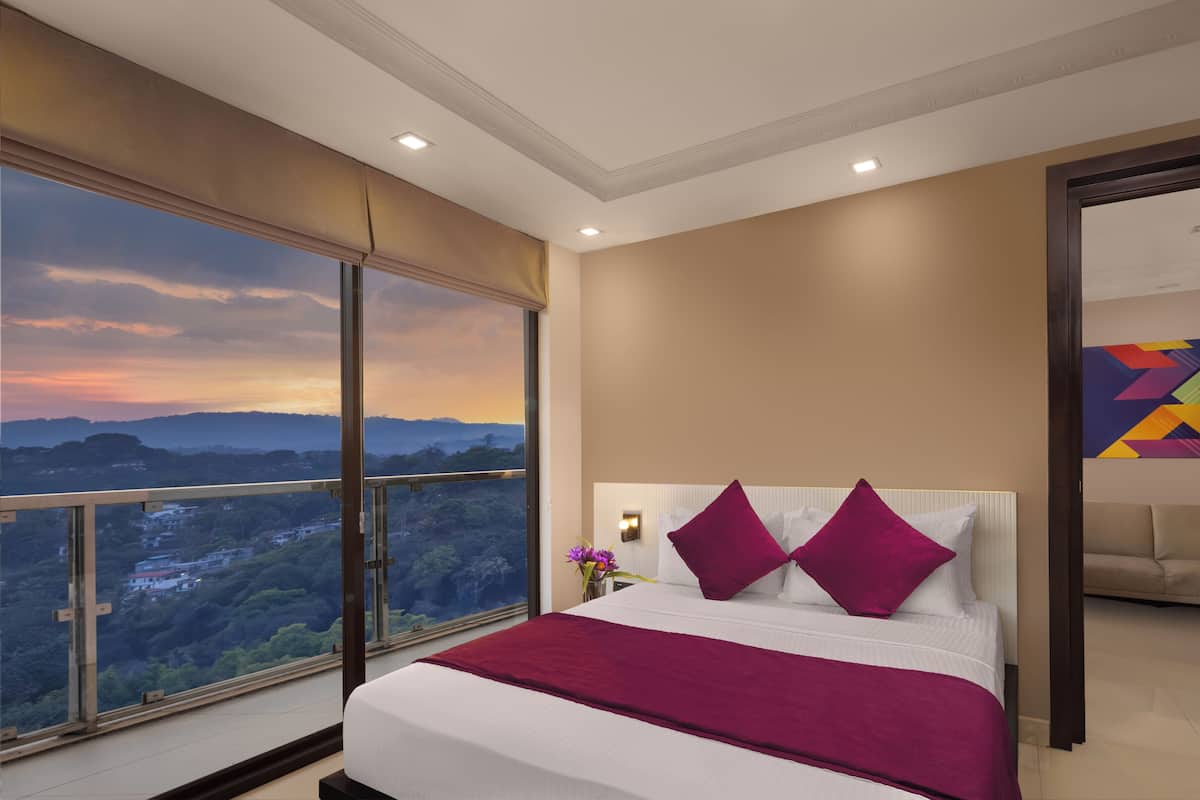 A modern hotel room with a large bed, a view of the mountains, and a colorful abstract painting on the wall.