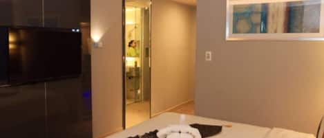 A hotel room with a bed, a TV, a painting, and a bathroom visible through an open door.