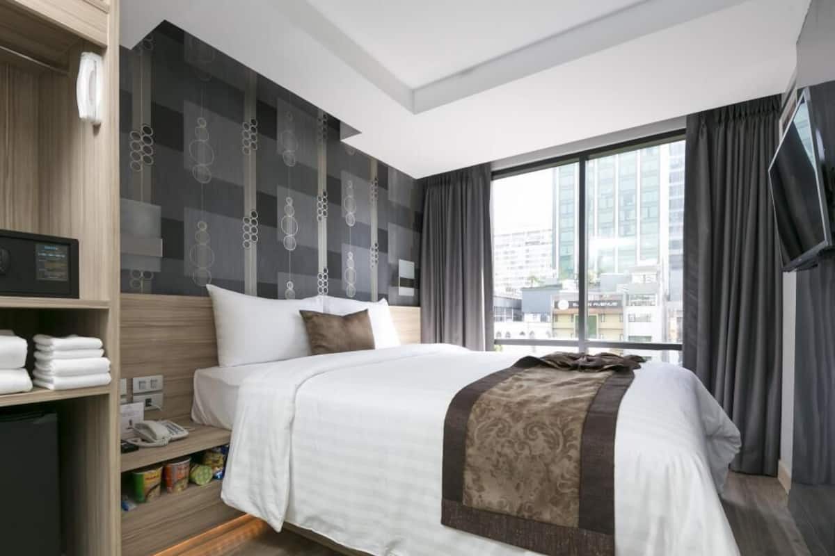 A hotel room with a large bed, a wardrobe, a desk with a telephone, and a window with a city view.