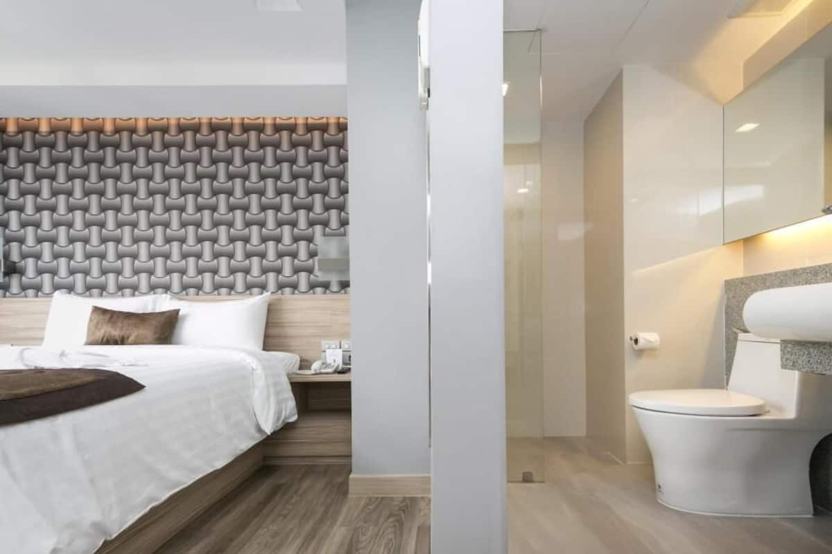 A modern hotel room with a bed, a nightstand, a bathroom with a toilet and sink, and a patterned wall.
