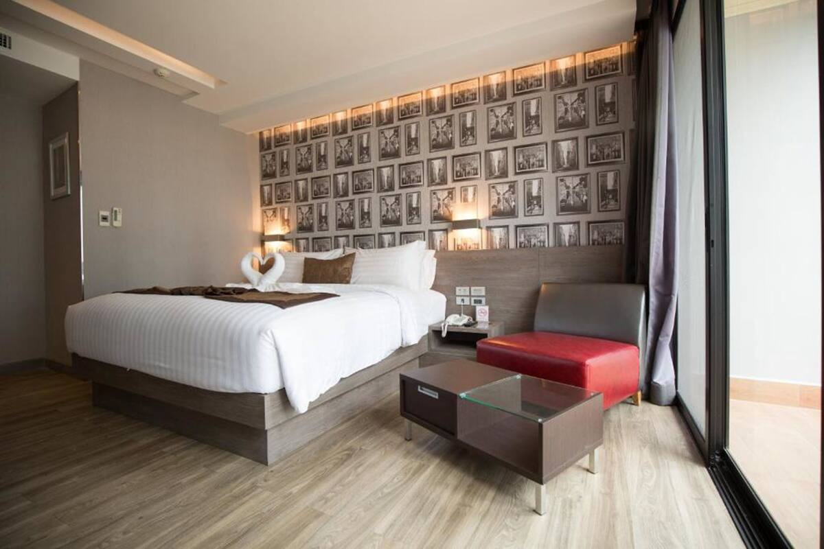 A modern hotel room with a large bed, a glass coffee table, a red sofa, and a wall decorated with framed pictures.