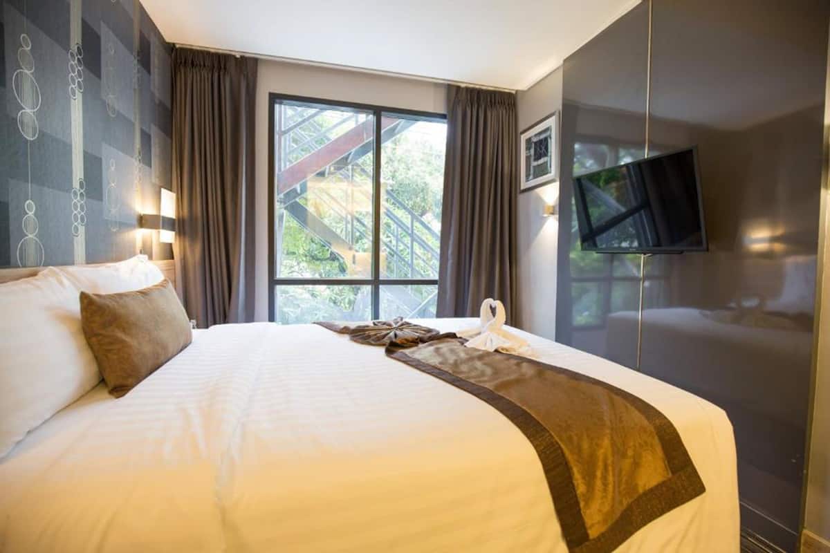 A hotel room with a large bed, a flat-screen TV mounted on the wall, and a window with a view of greenery.