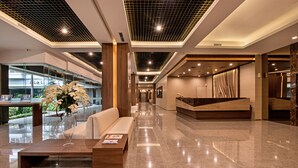 Eine moderne Hotellobby mit einer Rezeption, einer Sitzecke und einer Glaswand mit Blick ins Freie.