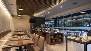 Ein moderner Essbereich mit langen Tischen, gepolsterten Stühlen und einer Buffetstation.
