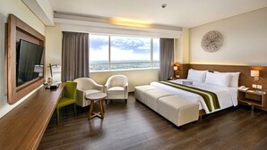 Ein Hotelzimmer mit einem großen Bett, einem Schreibtisch mit Stuhl, einem Fernseher und Blick auf die Stadt.