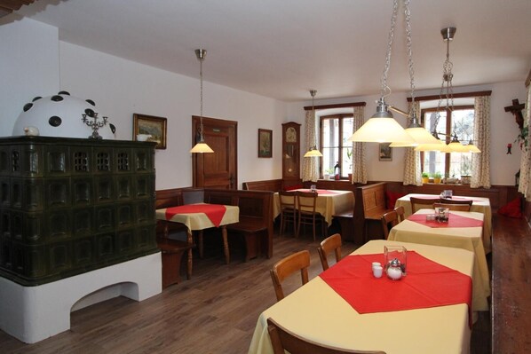 A dining area with wooden tables and chairs, a green cabinet, and hanging lamps.