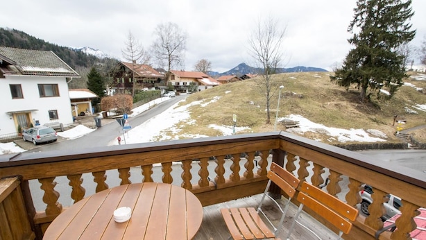 A wooden deck with a round table and benches, overlooking a residential area with houses and a road. - Gasthof Oberwirt (Fischbachau)