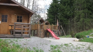 A wooden cabin with a playground featuring a red slide. - Gasthof Oberwirt (Fischbachau)