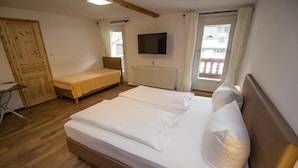 A bedroom with a large bed, a smaller bed, a wooden wardrobe, a radiator, and a TV on the wall. - Gasthof Oberwirt (Fischbachau)