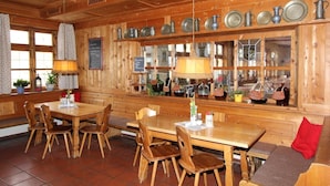 A wooden interior with a long dining table, multiple chairs, and a bench. There are shelves with various kitchenware and bottles. - Gasthof Oberwirt (Fischbachau)