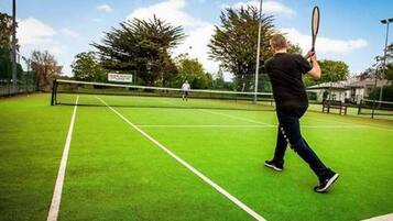 Un court de tennis avec un filet, des arbres et une personne qui joue au tennis.