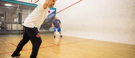 A squash court with wooden flooring and glass walls.