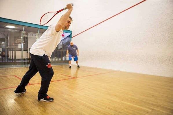 A squash court with wooden flooring and glass walls.