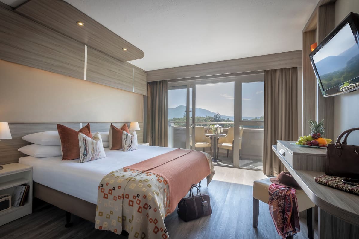 Ein Hotelzimmer mit einem großen Bett, einem Schreibtisch mit Fernseher, einem Balkon mit Blick und einer Obstschale.