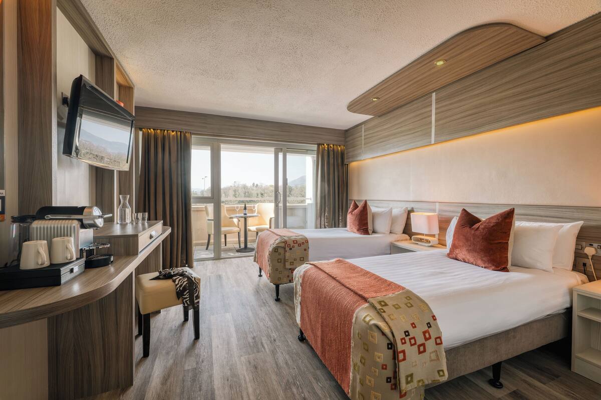 Ein Hotelzimmer mit zwei Betten, einem Schreibtisch mit Kaffeemaschine, einem Fernseher und Blick ins Freie.
