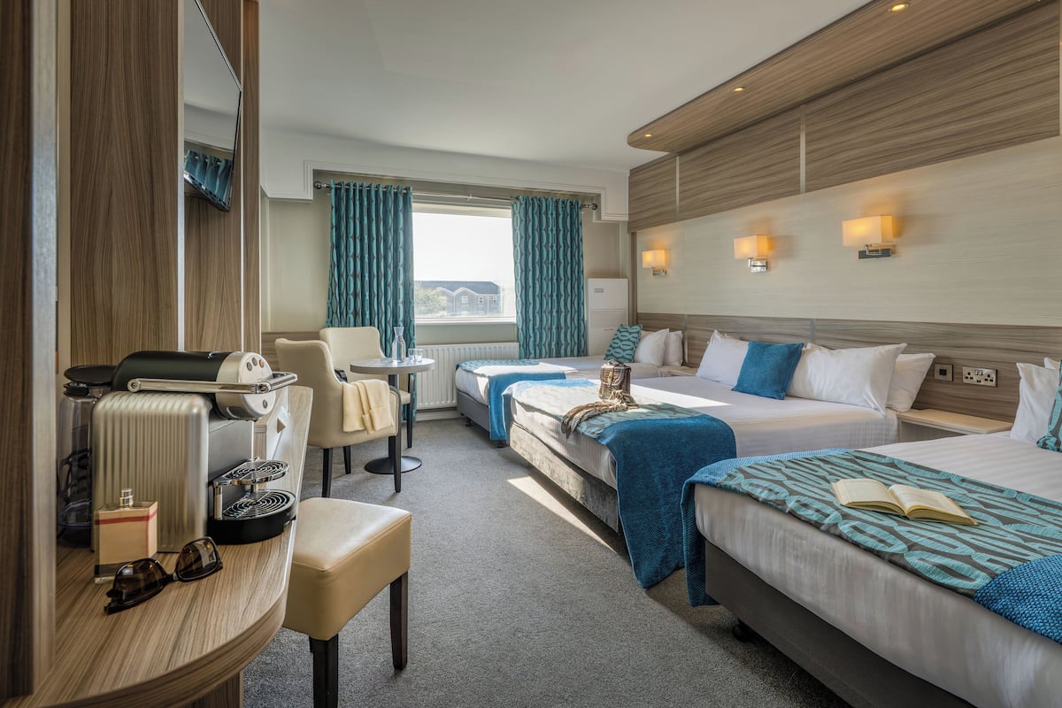 Ein Hotelzimmer mit zwei Betten, einem Schreibtisch mit Kaffeemaschine, einem Sessel und Blick nach draußen.