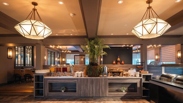 Un hall d’hôtel moderne avec un comptoir d’accueil central, un plancher en bois et des luminaires suspendus.