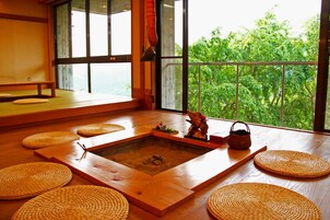 A traditional Japanese room with tatami flooring, a shoji screen, and a view of lush greenery.