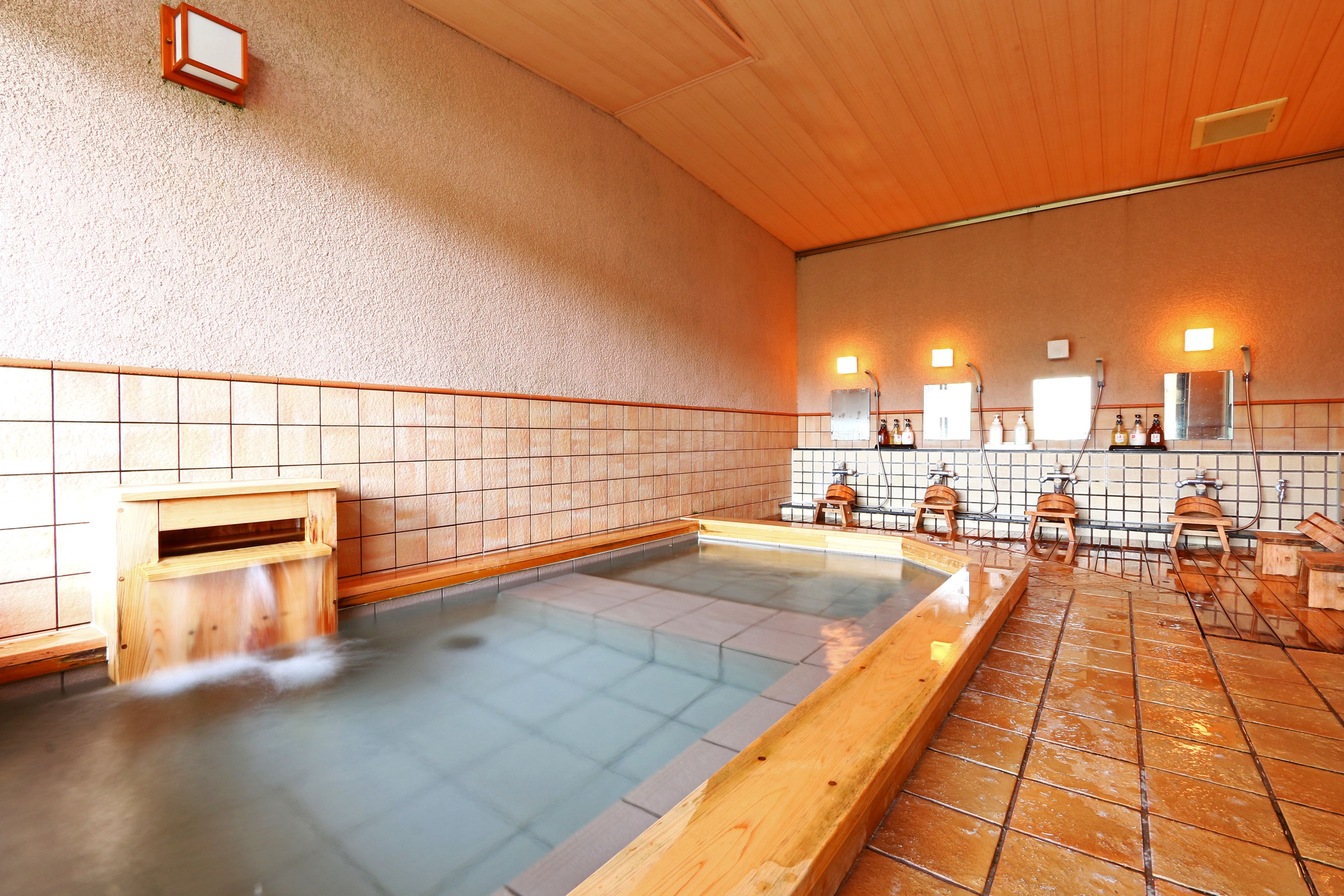 A traditional Japanese onsen with a wooden bath, tiled walls, and a tiled floor.