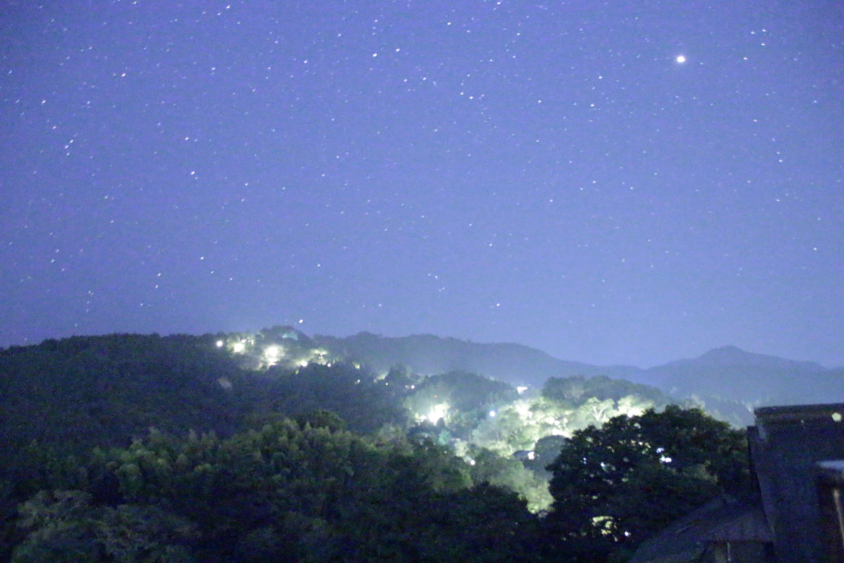 Cielo nocturno con estrellas y un paisaje urbano al fondo.