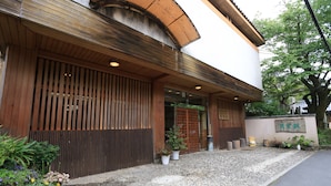 A traditional Japanese building with a wooden facade, a gravel entrance, and potted plants. - Hounkan (Yoshino)