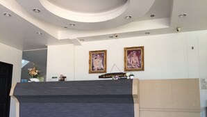 Una recepción con un panel gris oscuro, dos retratos enmarcados en la pared y una planta pequeña en el mostrador.