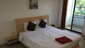Una cama bien hecha con sábanas blancas y dos almohadas oscuras, una mesita de noche con un teléfono y un cuadro en la pared.