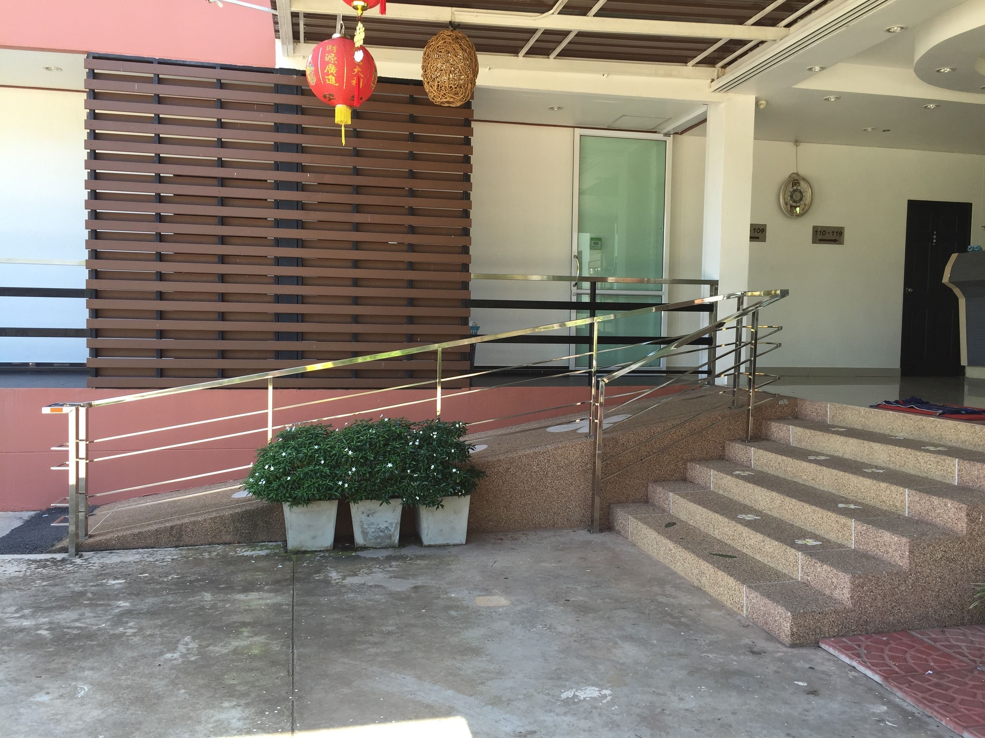 Una escalera con barandillas metálicas que lleva a un espacio interior, un farolillo rojo y plantas en macetas.
