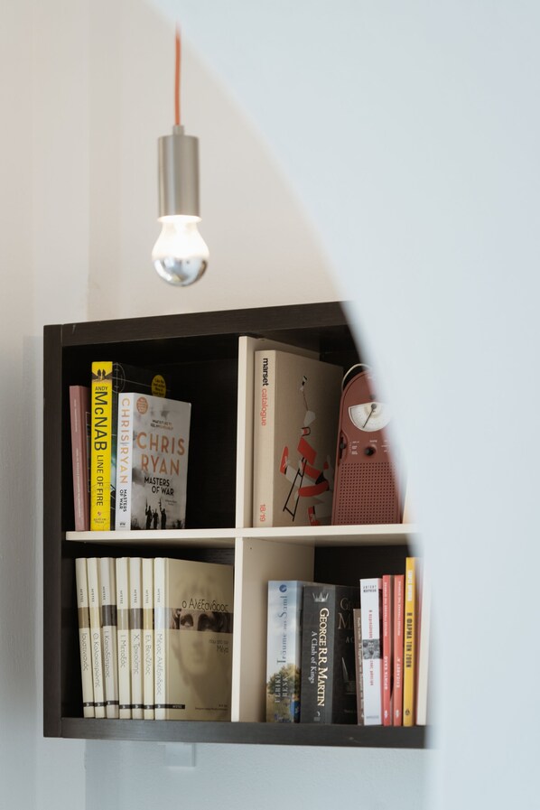 A bookshelf with various books, a lamp, and a clock. - Le Grand Blue (Santorini)