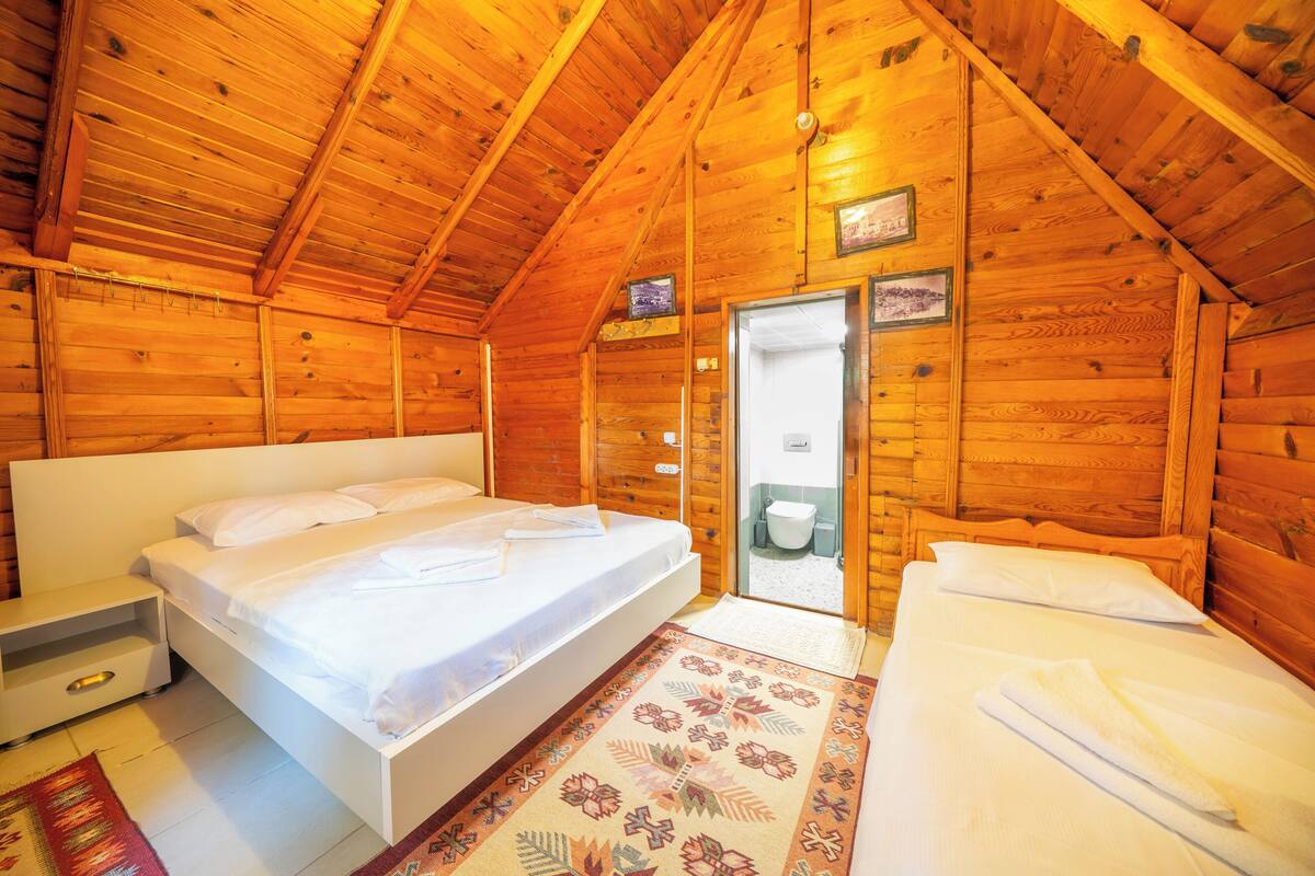 Un dormitorio de cabaña de madera con una cama individual, una mesita de noche, una pequeña mesa y una puerta que da a un baño.