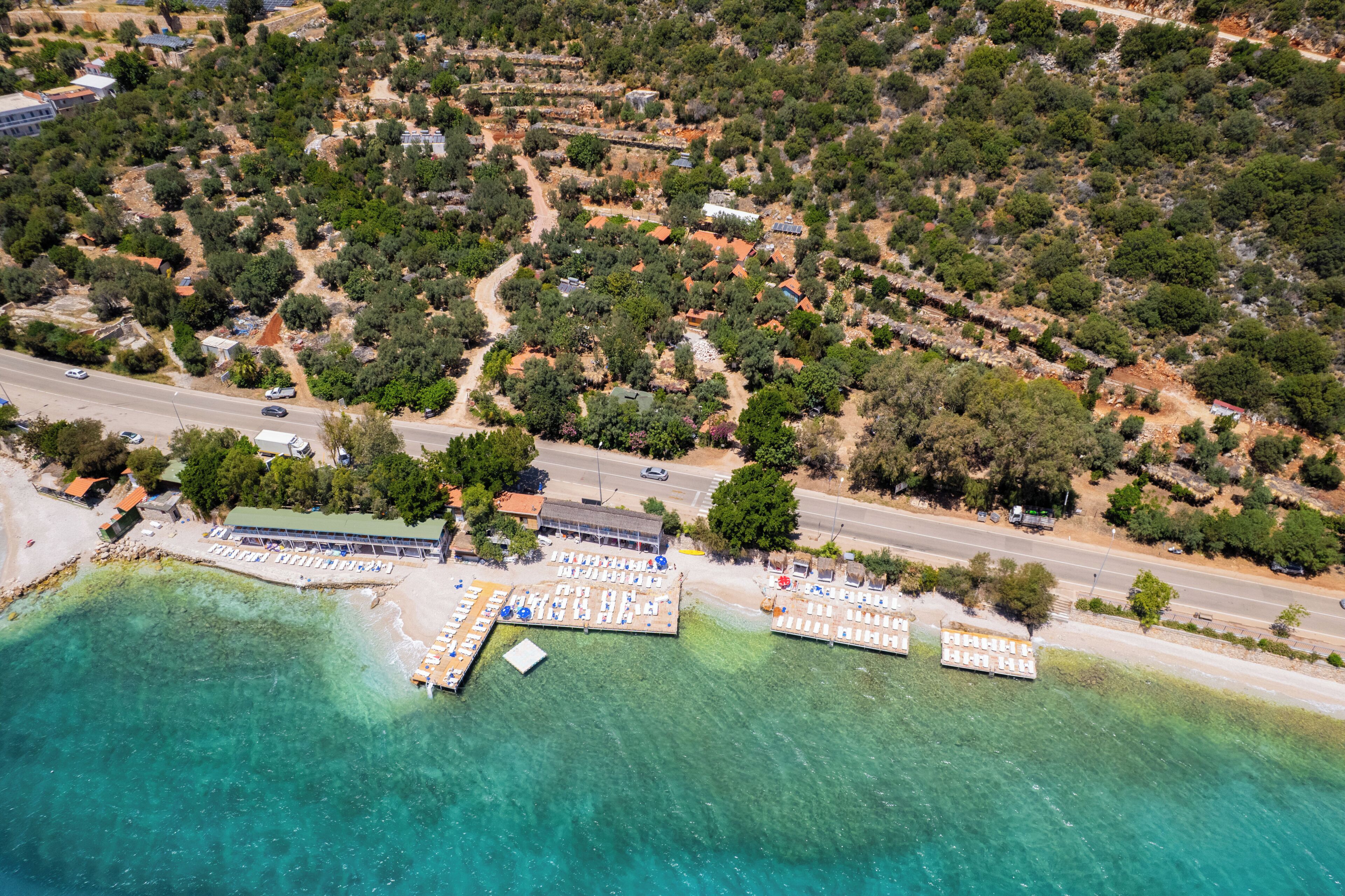Ein Luftbild einer Küstenlandschaft mit Strand, klarem türkisblauem Wasser und einem Steg mit Liegestühlen.