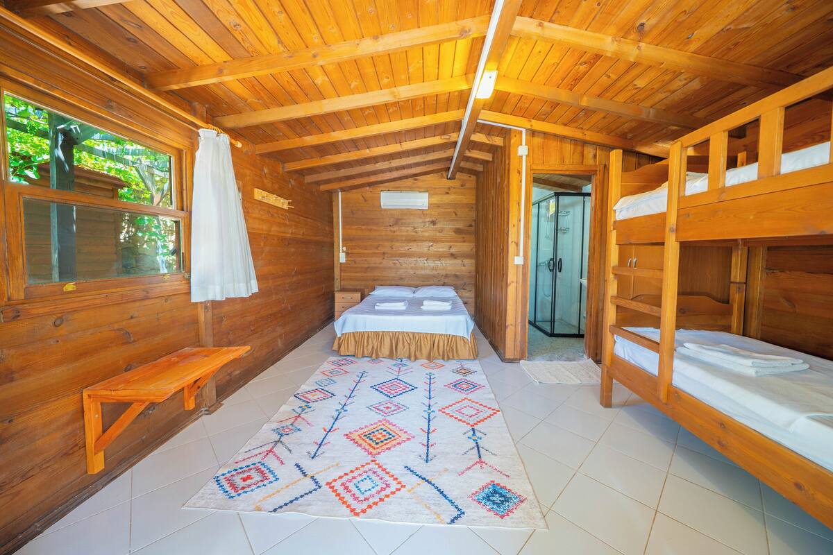 Una cabaña de madera con literas, una cama individual, un banco y una alfombra estampada.
