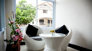 A room with two white wicker chairs with black cushions, a small white table, and a vase with flowers. - The Room (Udon Thani)