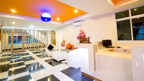 A reception area with a checkered floor, white sofas, a reception desk, and a staircase leading to an upper level. - The Room (Udon Thani)