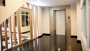 A modern interior with a polished floor, a staircase with glass railings, and a door with a textured wall. - The Room (Udon Thani)