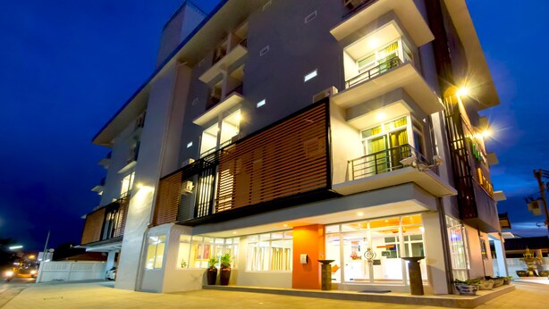 A multi-story hotel with a modern design, featuring balconies, a ground-level entrance, and illuminated windows. - The Room (Udon Thani)
