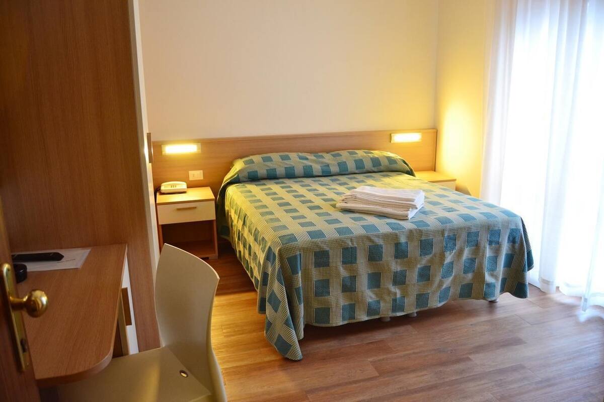 A hotel room with a bed, bedside tables, a chair, and a desk.