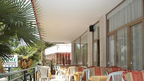Un espace extérieur abrité, doté de tables et de chaises, d’un sol carrelé et d’une rambarde.