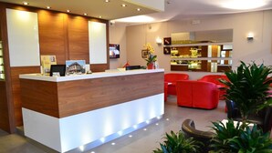 Un espace d’accueil d’hôtel avec un comptoir de réception en bois, des sièges rouges et un bar en arrière-plan.