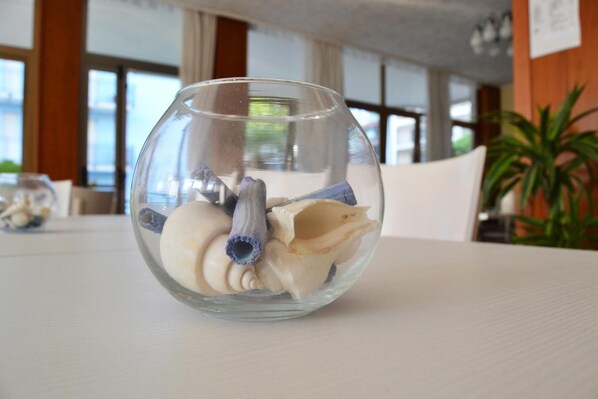 A clear glass bowl on a table with various seashells and a conch shell.