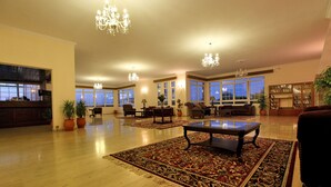 A spacious living room with large windows, multiple seating areas, and a chandelier. - Belvedere Aeolis Hotel (Lesvos)